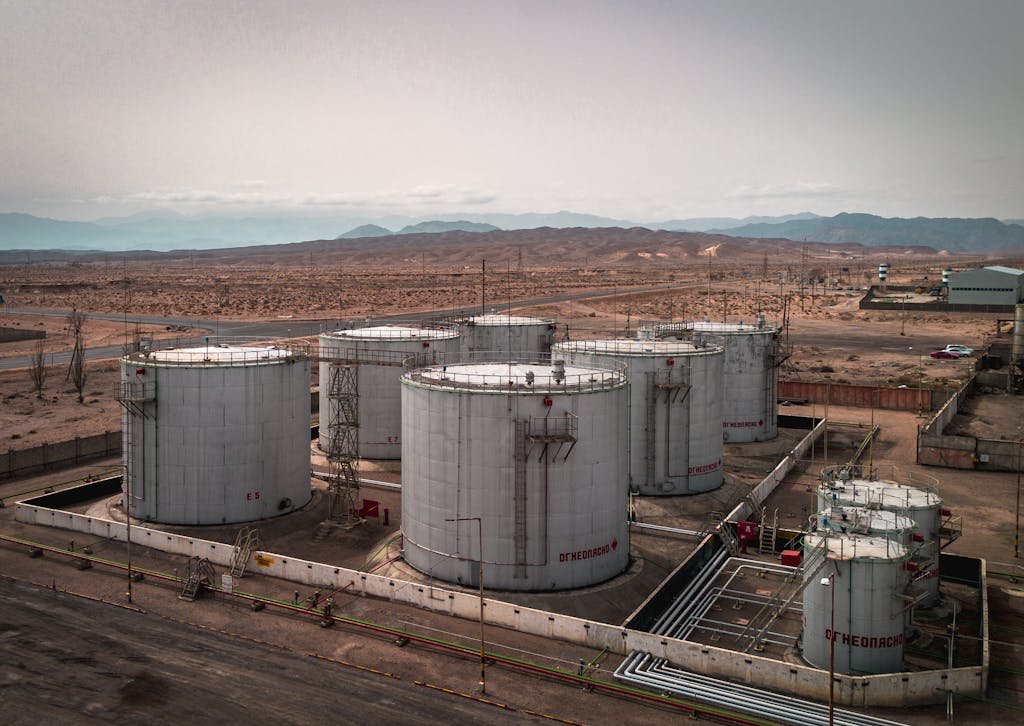 Aerial view of large industrial oil tanks in a desert setting with mountains in the distance.