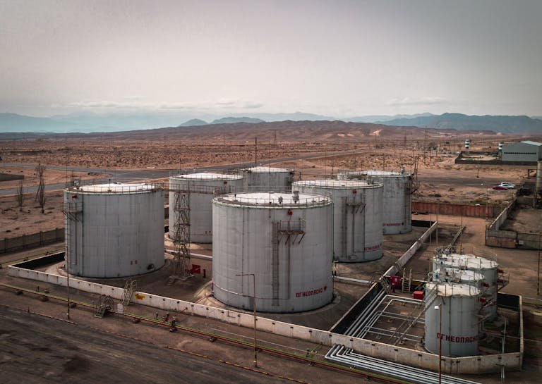 Aerial view of large industrial oil tanks in a desert setting with mountains in the distance.